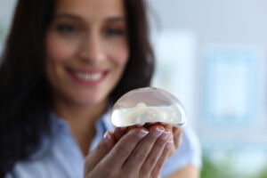 Focus on breast silicone implants in female hands. Happy cheerful brunette looking at transparent breast with gladness. Plastic surgeons and anaplasty concept