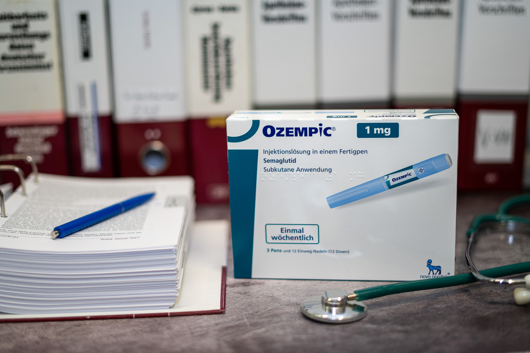 A Drug box of Ozempic containing Semaglutide for treatment of type 2 diabetes and long-term weight management on a table and in the background different medical books.