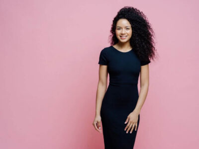 Woman in a black dress posing against a pink backdrop - Michelle Hardaway M.D.