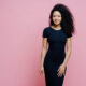 Woman in a black dress posing against a pink backdrop - Michelle Hardaway M.D.