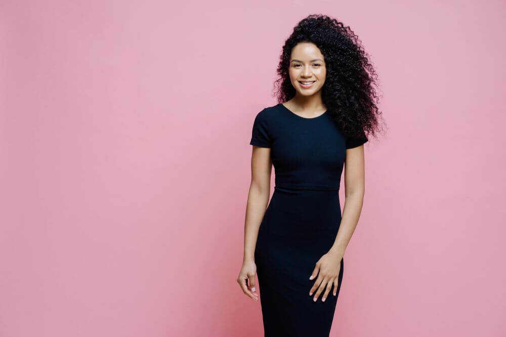 Woman in a black dress posing against a pink backdrop - Michelle Hardaway M.D.